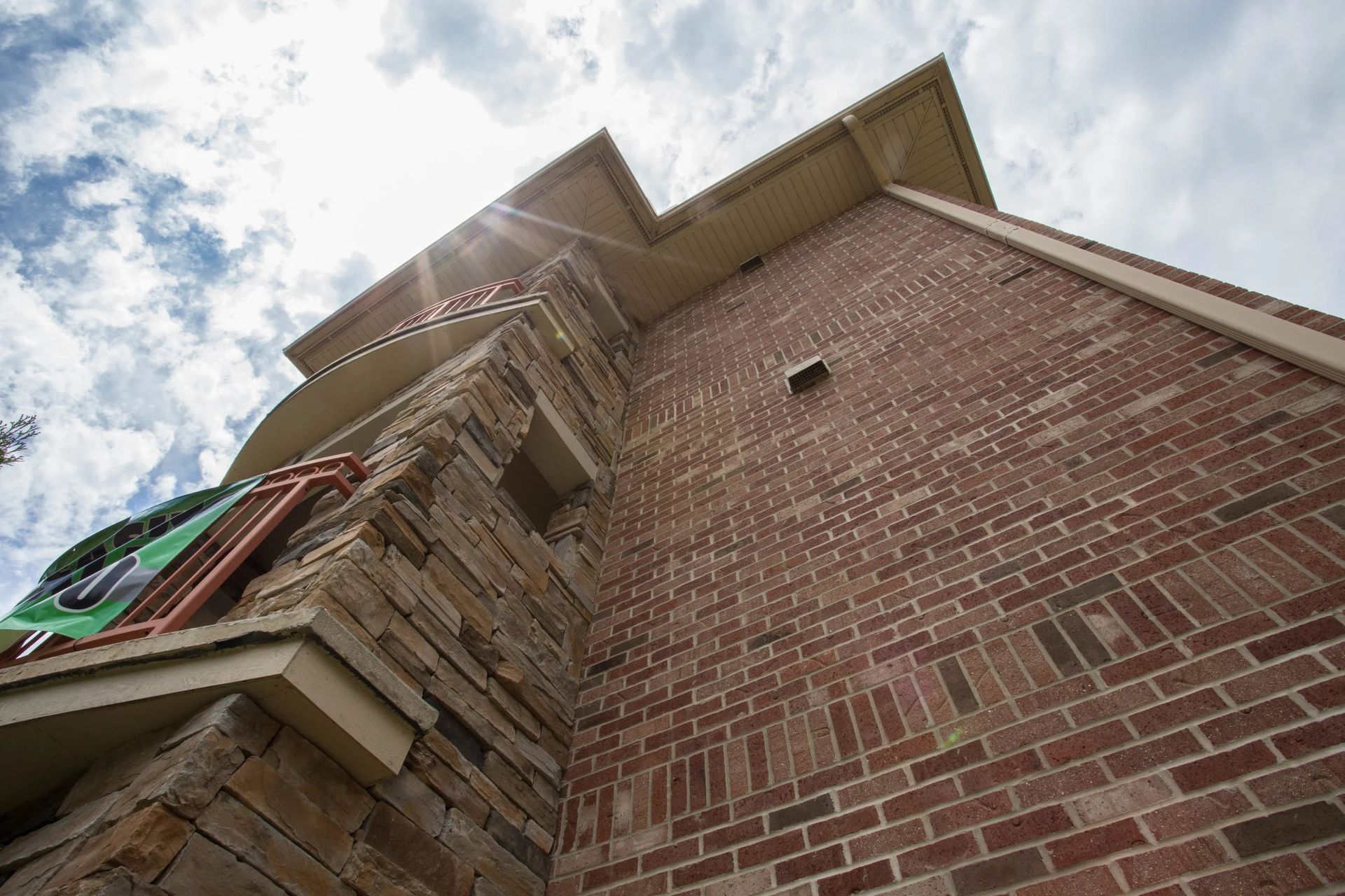 Low-angle view of a brick building facade with a balcony, roof overhang, and blue sky with clouds