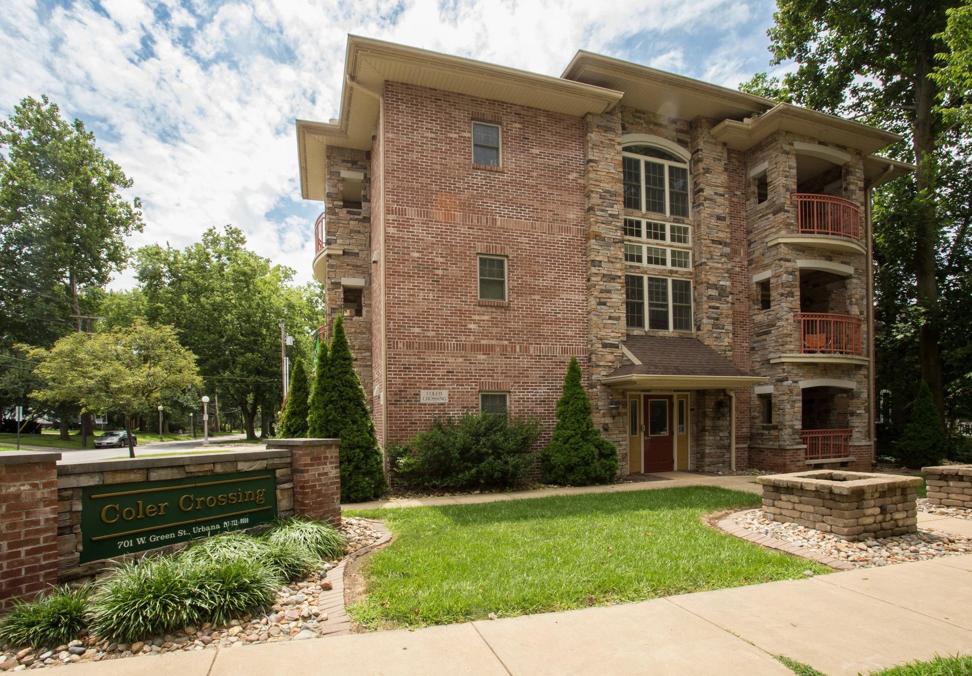 Brick apartment building with balconies and a green lawn under a partly cloudy sky