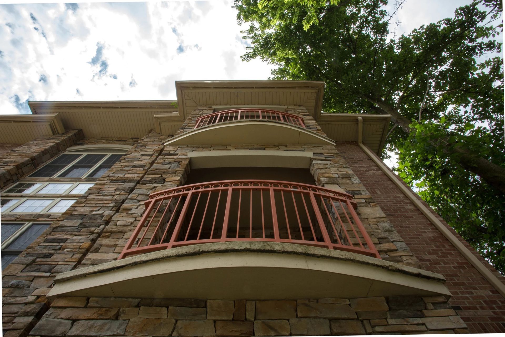 Low-angle view of a brick building with red balconies and trees above