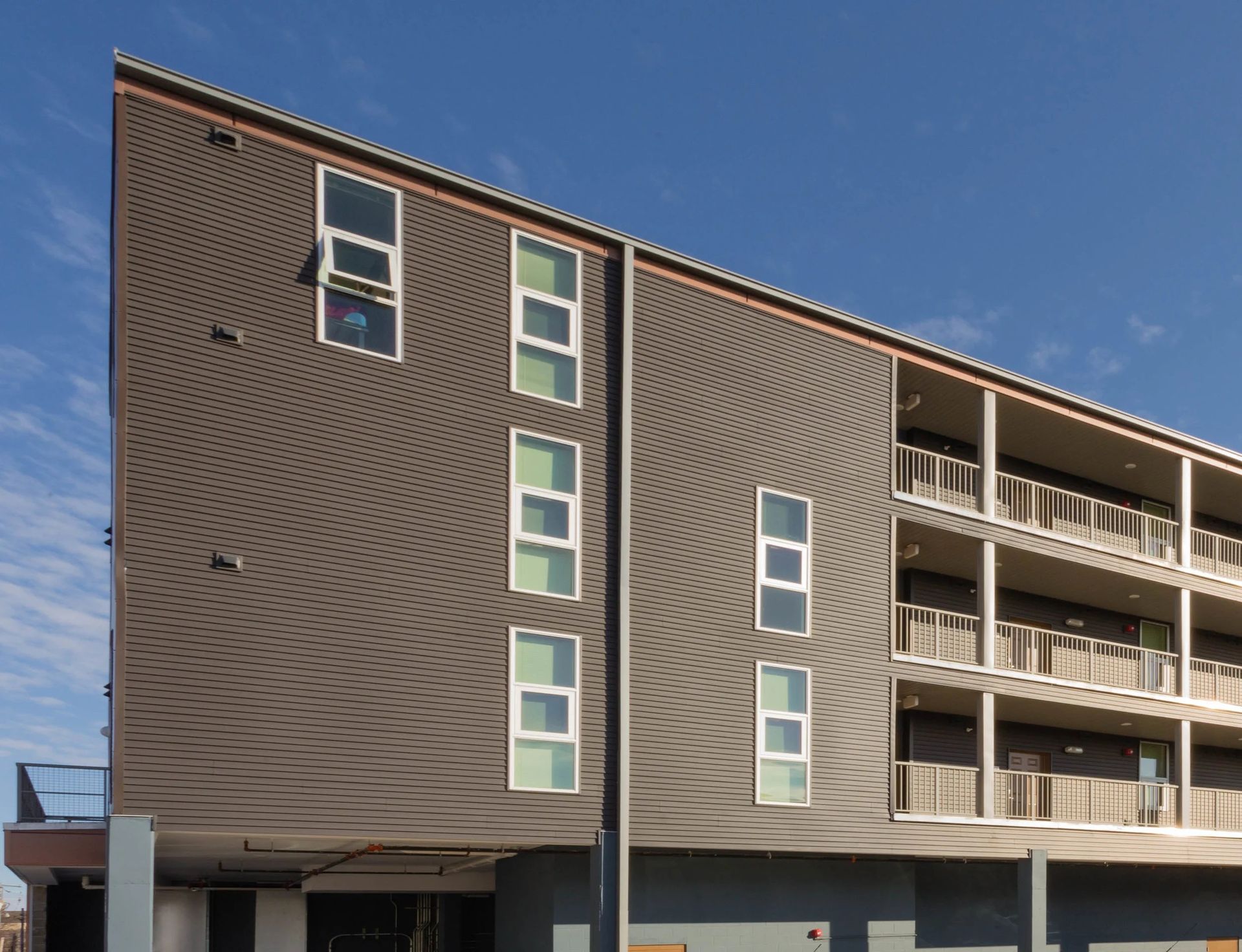 Modern apartment building exterior with brown siding, vertical windows, and balconies under a blue sky