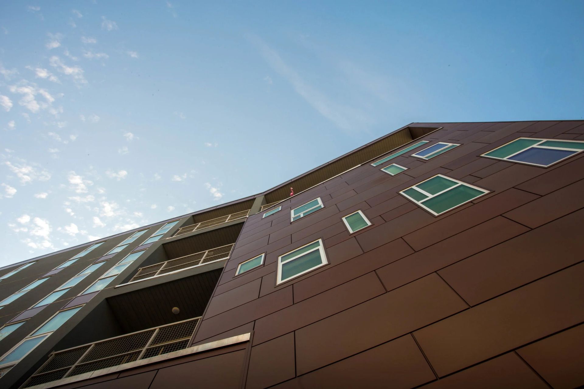 Low-angle view of a brown apartment building with green-trimmed windows against a blue sky