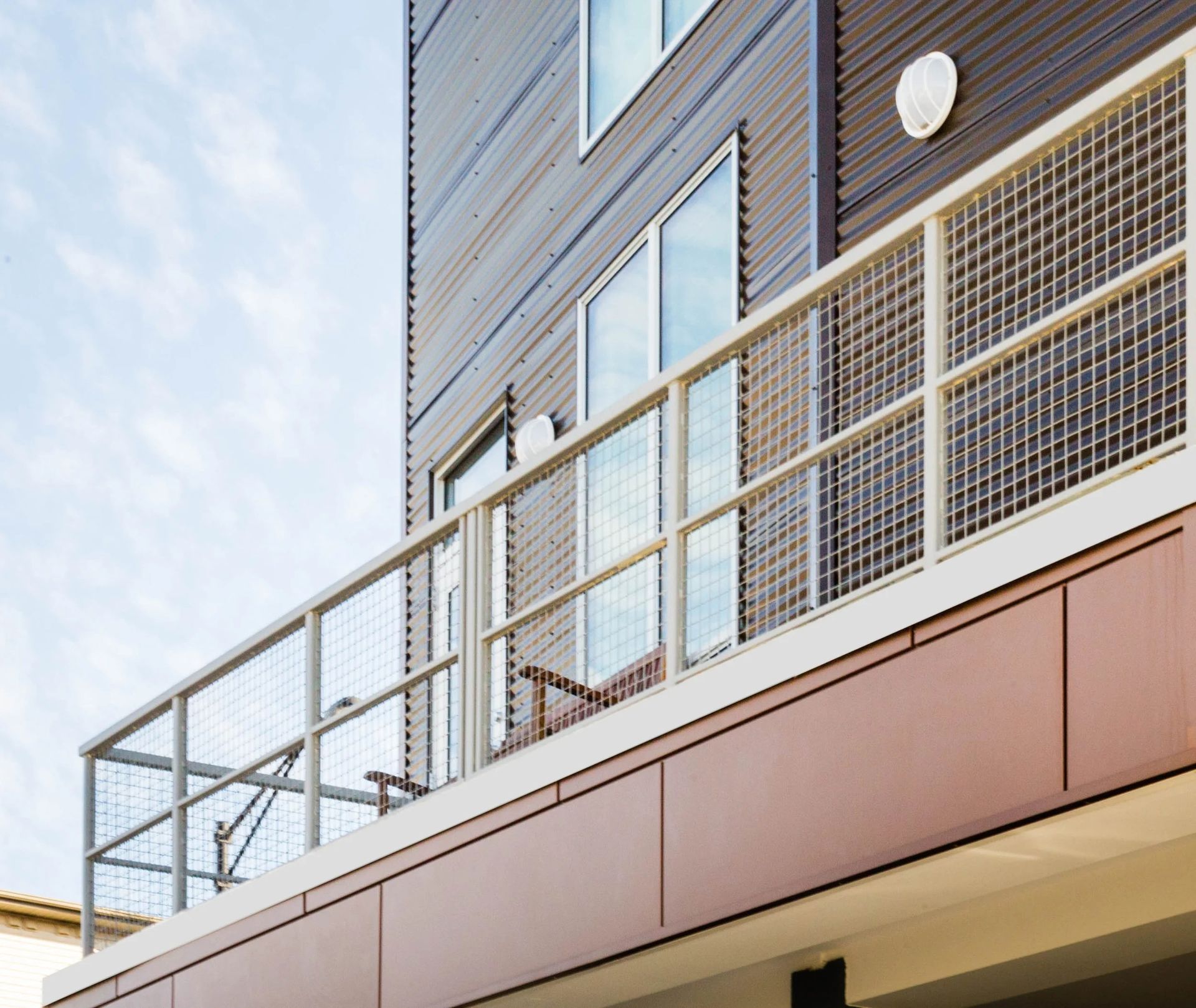 Modern building exterior with a metal-railed balcony and light blue sky above