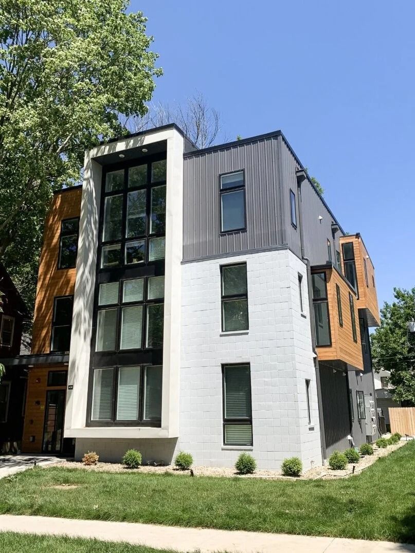 Modern multi-story apartment building with white and dark gray siding, large windows, and a grassy front yard
