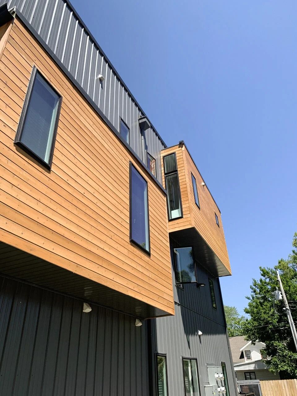 Modern townhouse exterior with orange wood siding, black panels, and windows against a clear blue sky