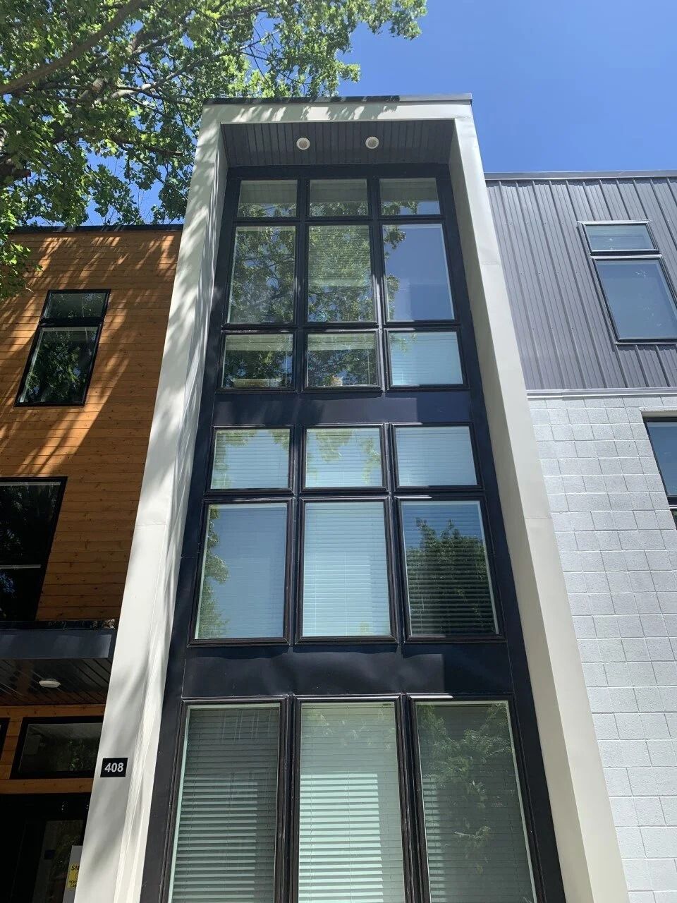 Modern three-story townhouse with tall black-framed windows and a tree reflected in the glass