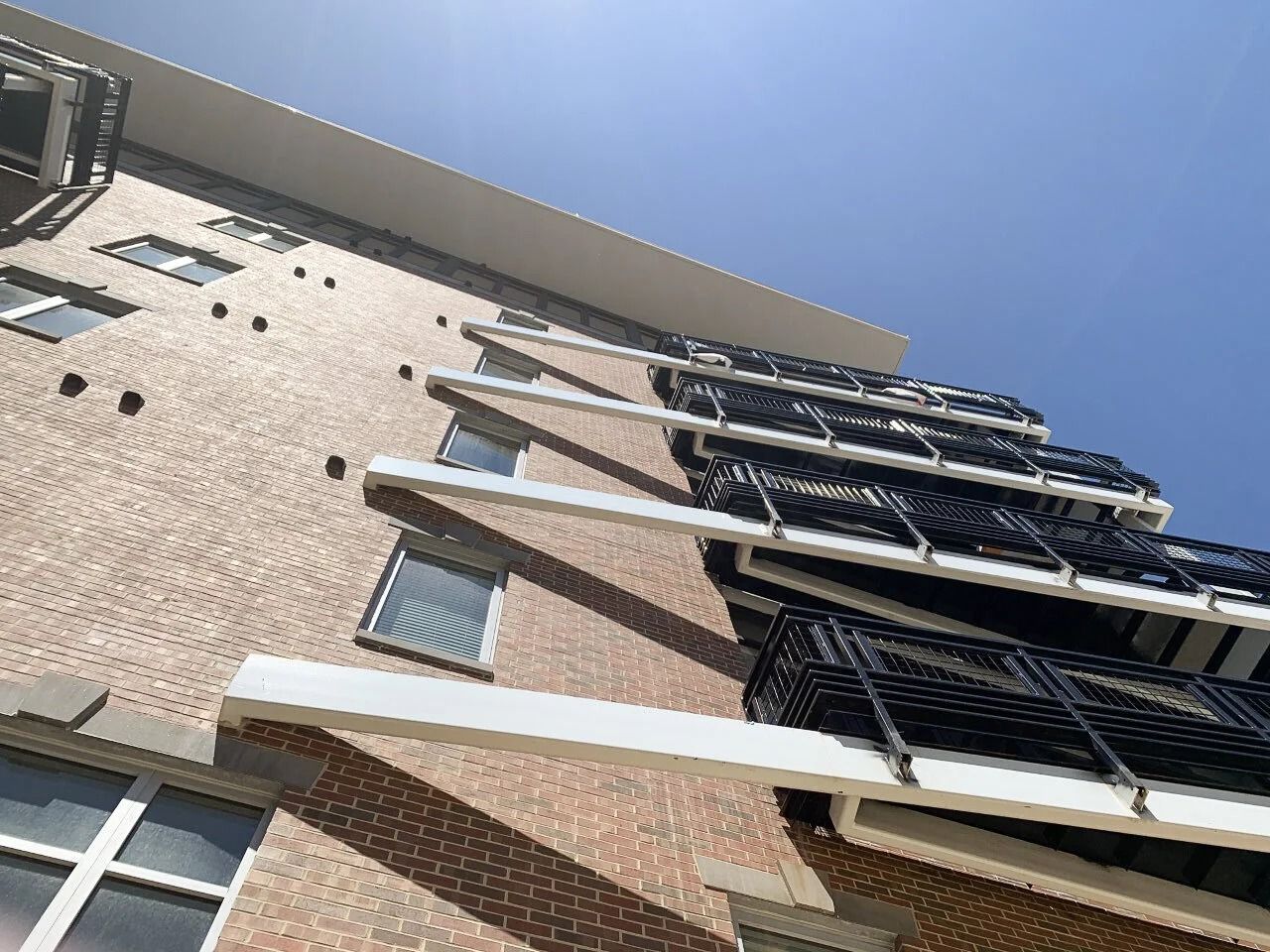 Low-angle view of a brick apartment building with balconies against a blue sky