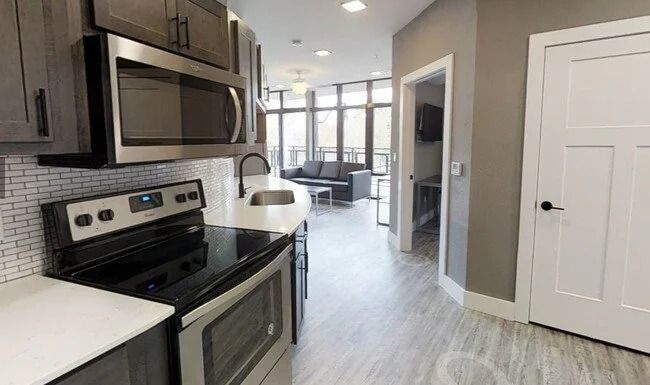 Modern kitchen with stainless steel appliances, white cabinets, and a bright dining area beyond.