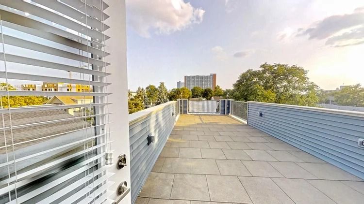Modern rooftop terrace with gray tile floor, blue railing, and city view at sunset