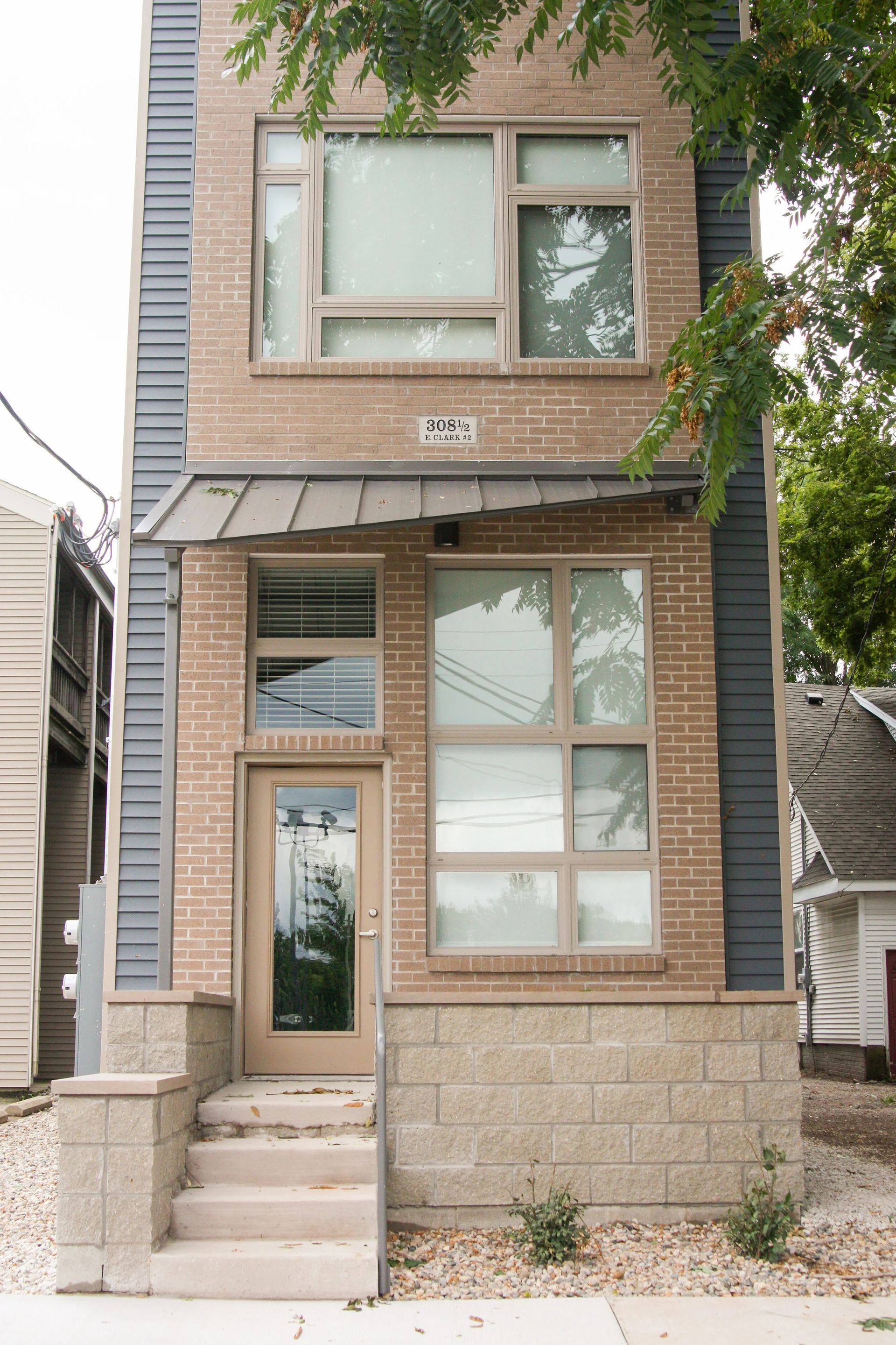 Narrow two-story brick townhouse with large windows and a small front stoop, viewed from the street