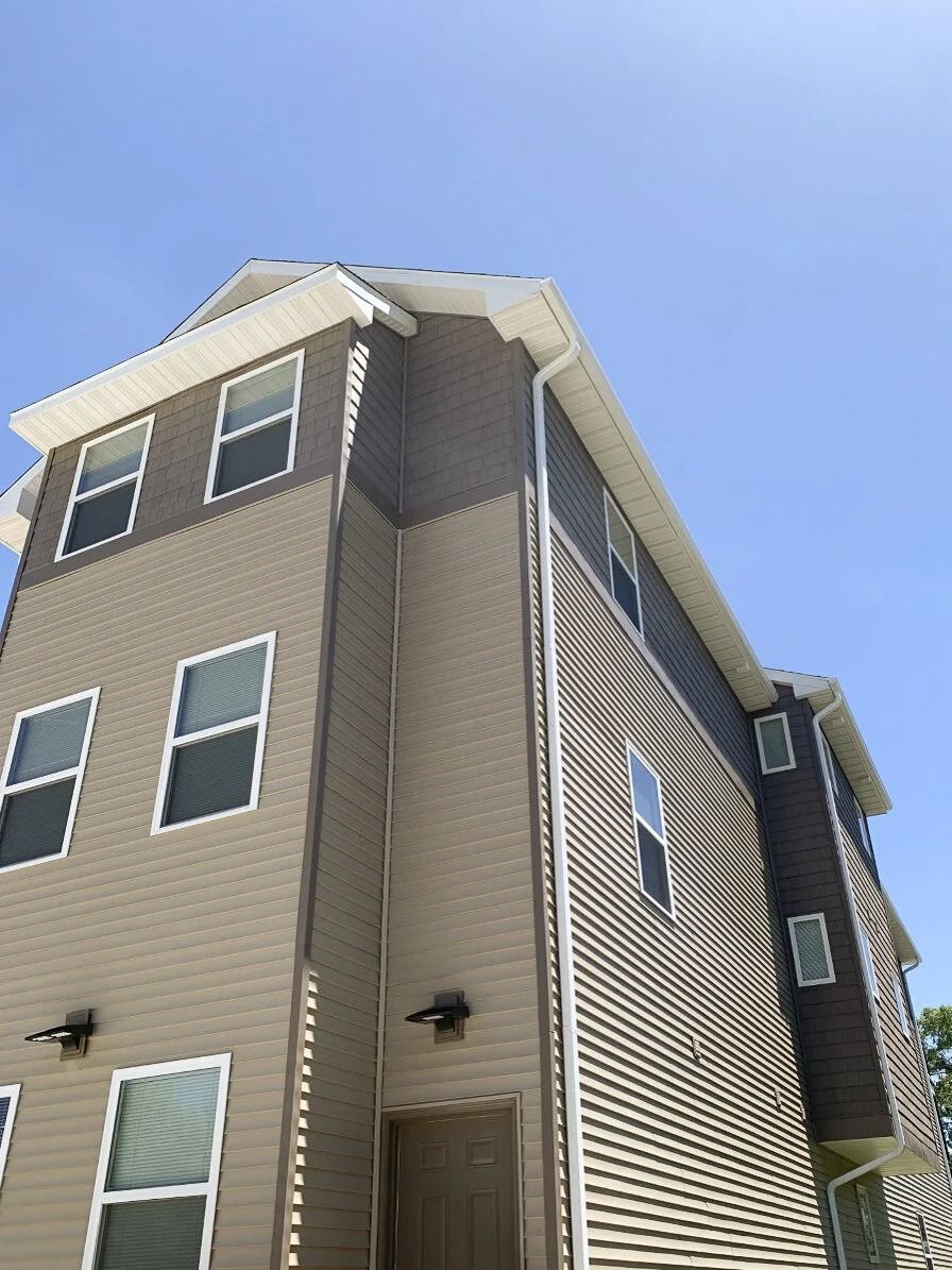 Tall tan apartment building with white trim viewed from below against a blue sky