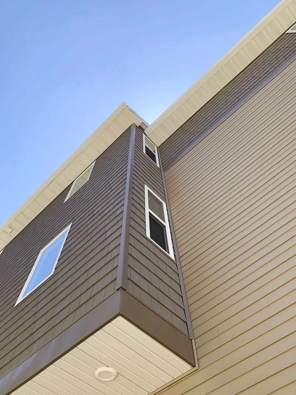 Corner view of a brown house exterior with white-trimmed windows against a clear blue sky