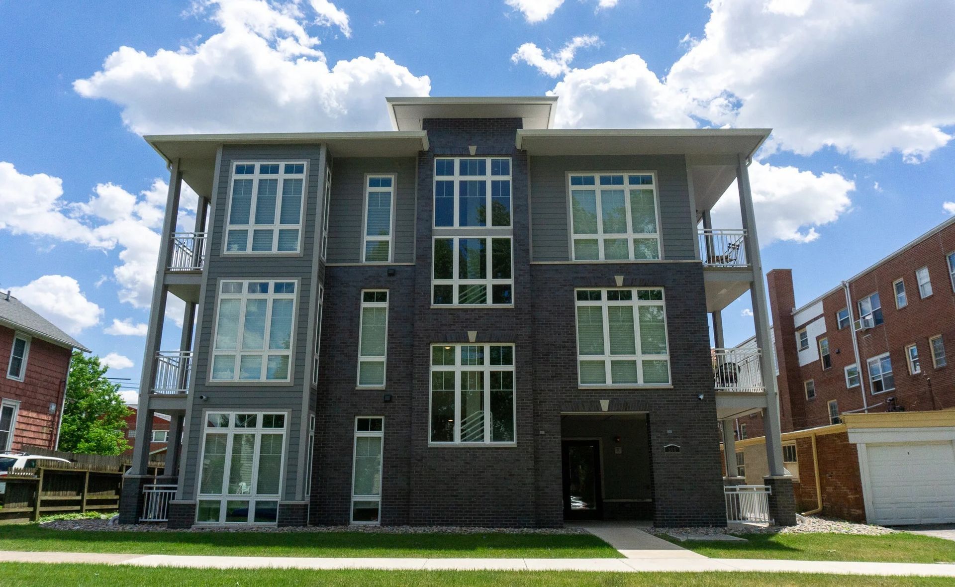 Modern three-story gray apartment building with large windows under a blue sky