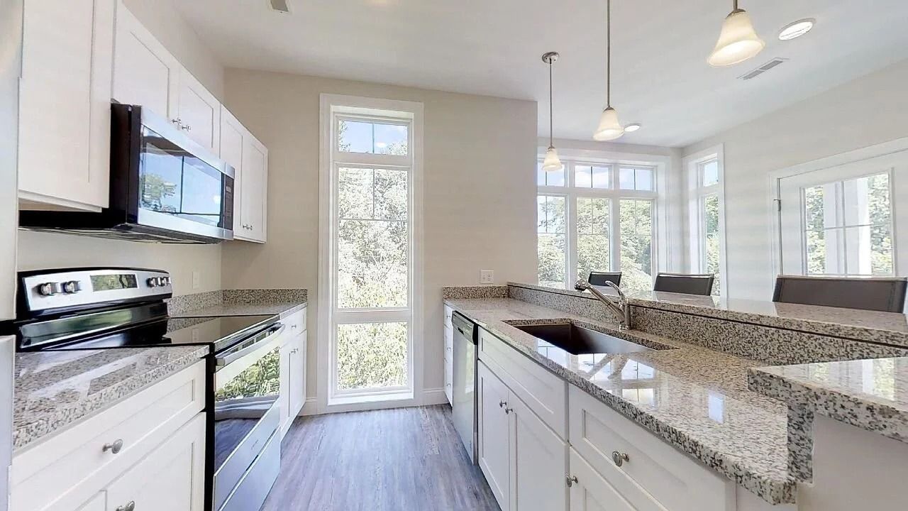 Bright modern kitchen with white cabinets, granite island, stainless stove, and tall windows