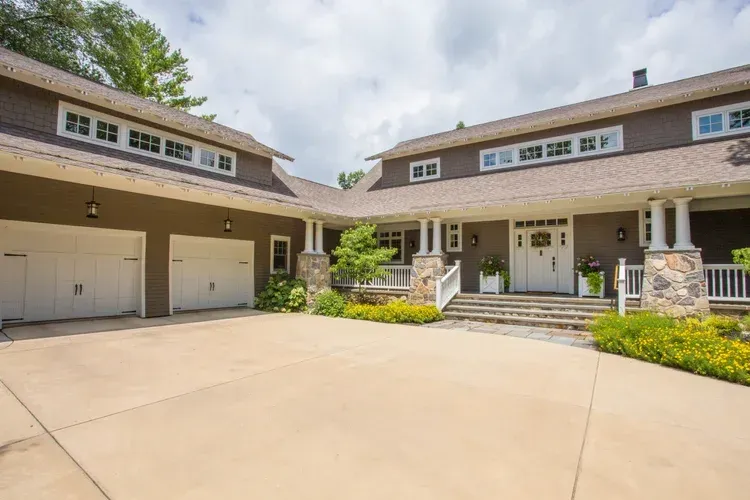 Spacious suburban home with two garage doors, front porch, and large driveway under a cloudy sky