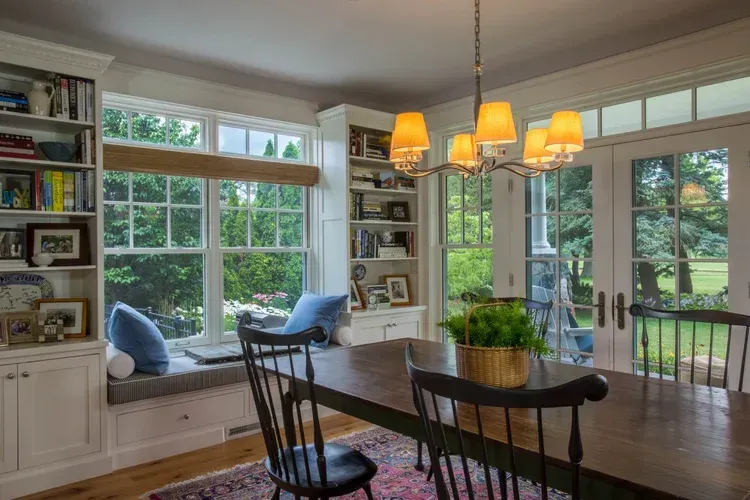 Bright sunroom dining area with large windows, a built-in window seat, and a hanging chandelier