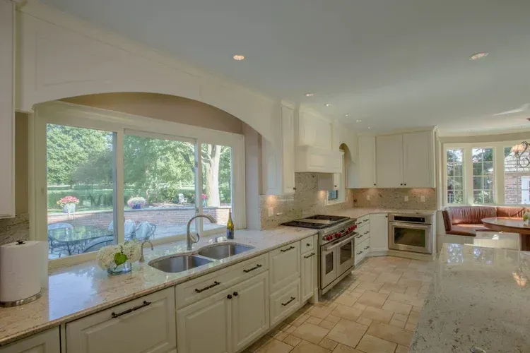 Bright modern kitchen with white cabinets, large island, and wide window overlooking a pool
