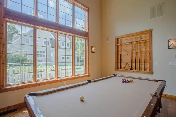 Bright game room with a pool table, large windows, and a wall-mounted cue rack