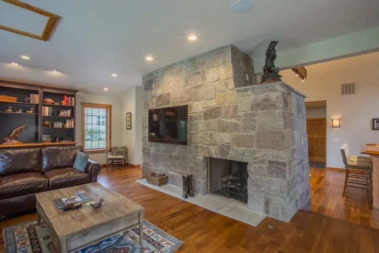 Cozy living room with leather sofa, stone fireplace, hardwood floors, and built-in shelves