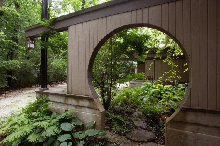 Wooden garden bridge with a circular opening spanning lush greenery and ferns
