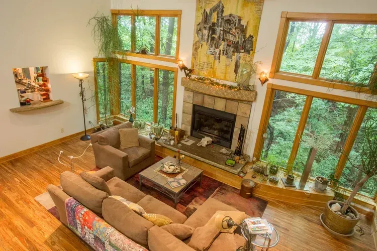 Spacious living room with a stone fireplace, large windows, sectional sofa, and hardwood floors