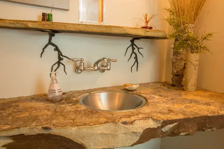 Stone bathroom vanity with a round sink, rustic shelf, and decorative branches above the faucet