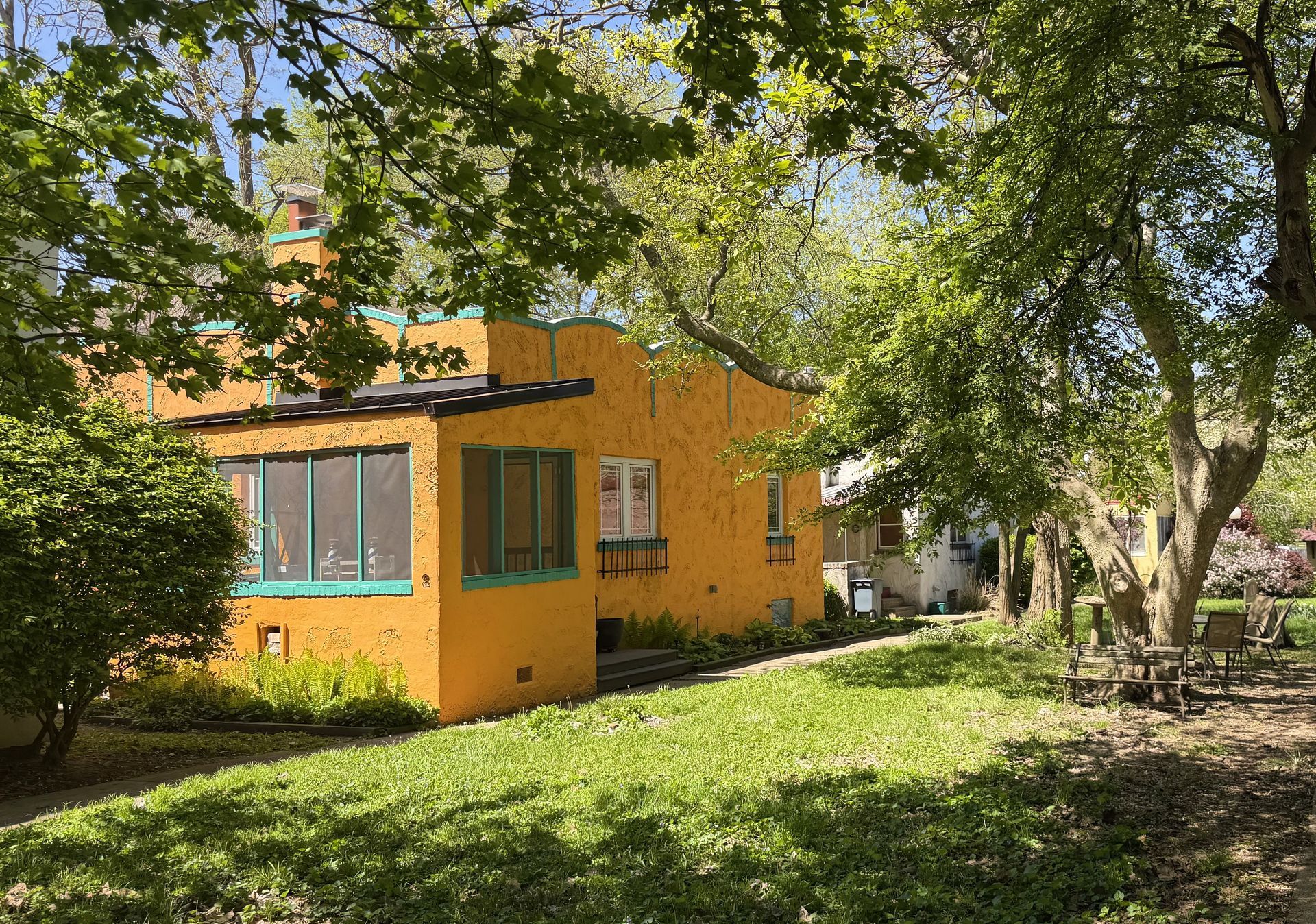 Orange house with blue-trimmed windows in a leafy garden under trees
