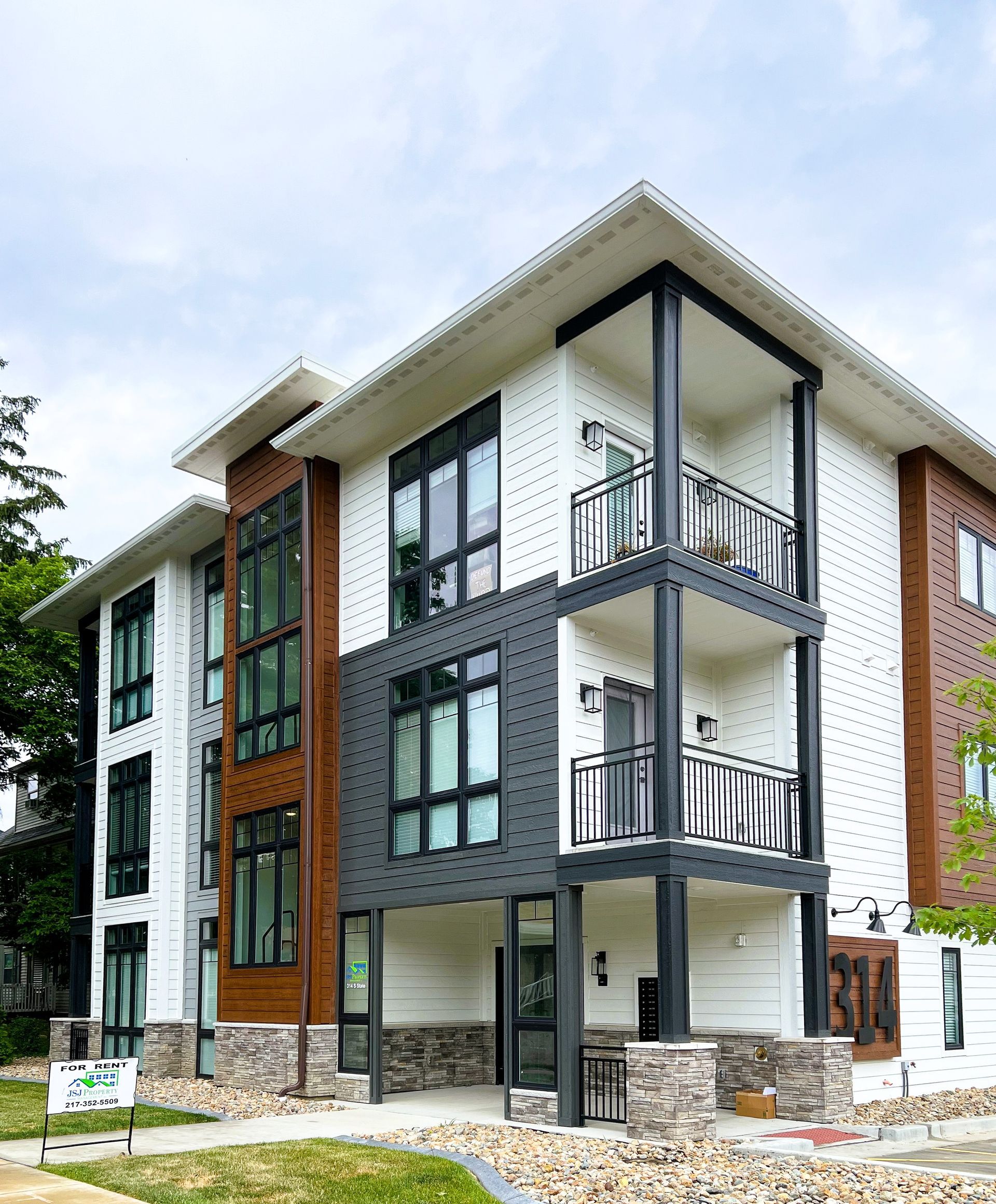 Modern three-story apartment building with gray and white exterior, balconies, and brick accents under construction