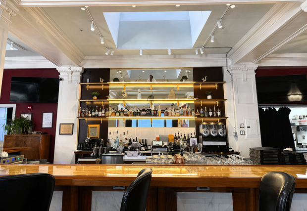 Empty upscale bar with polished wood counter, backlit shelves, and white coffered ceiling.