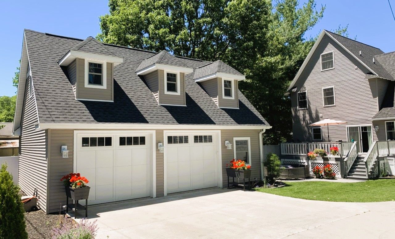 Suburban house with two white garage doors, dormer windows, and a landscaped driveway under a blue sky