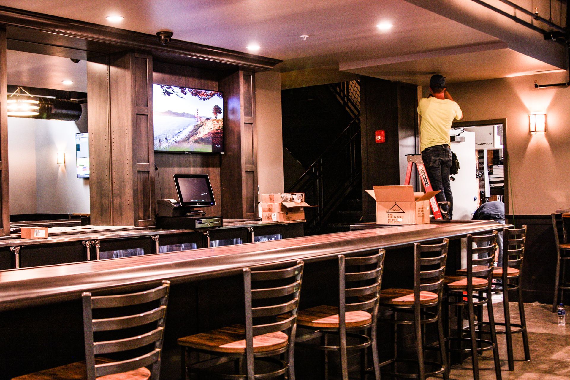 Empty restaurant bar with stools and a worker cleaning behind the counter