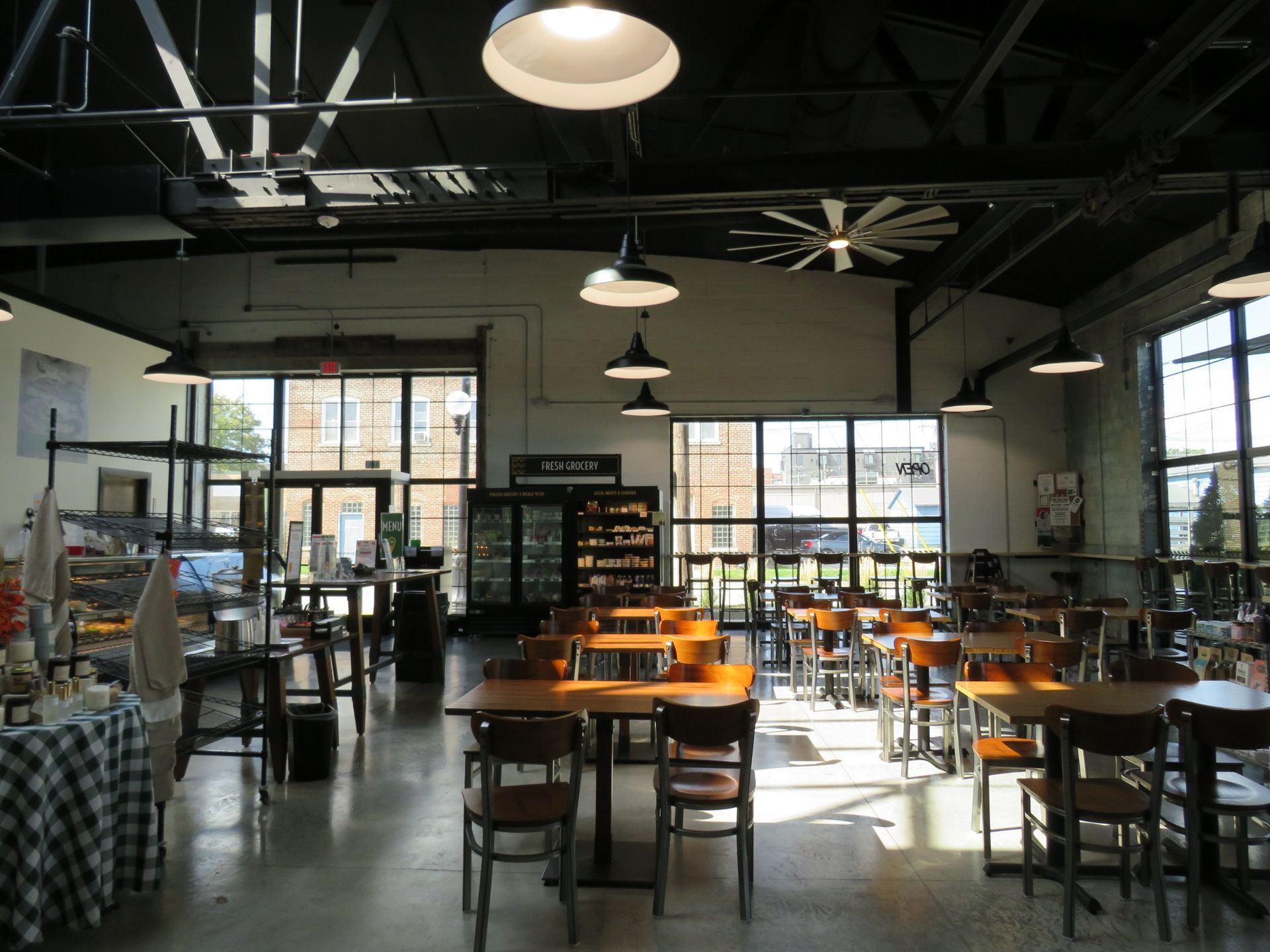 Spacious industrial-style café with wooden tables, chairs, hanging lights, and large sunlit windows