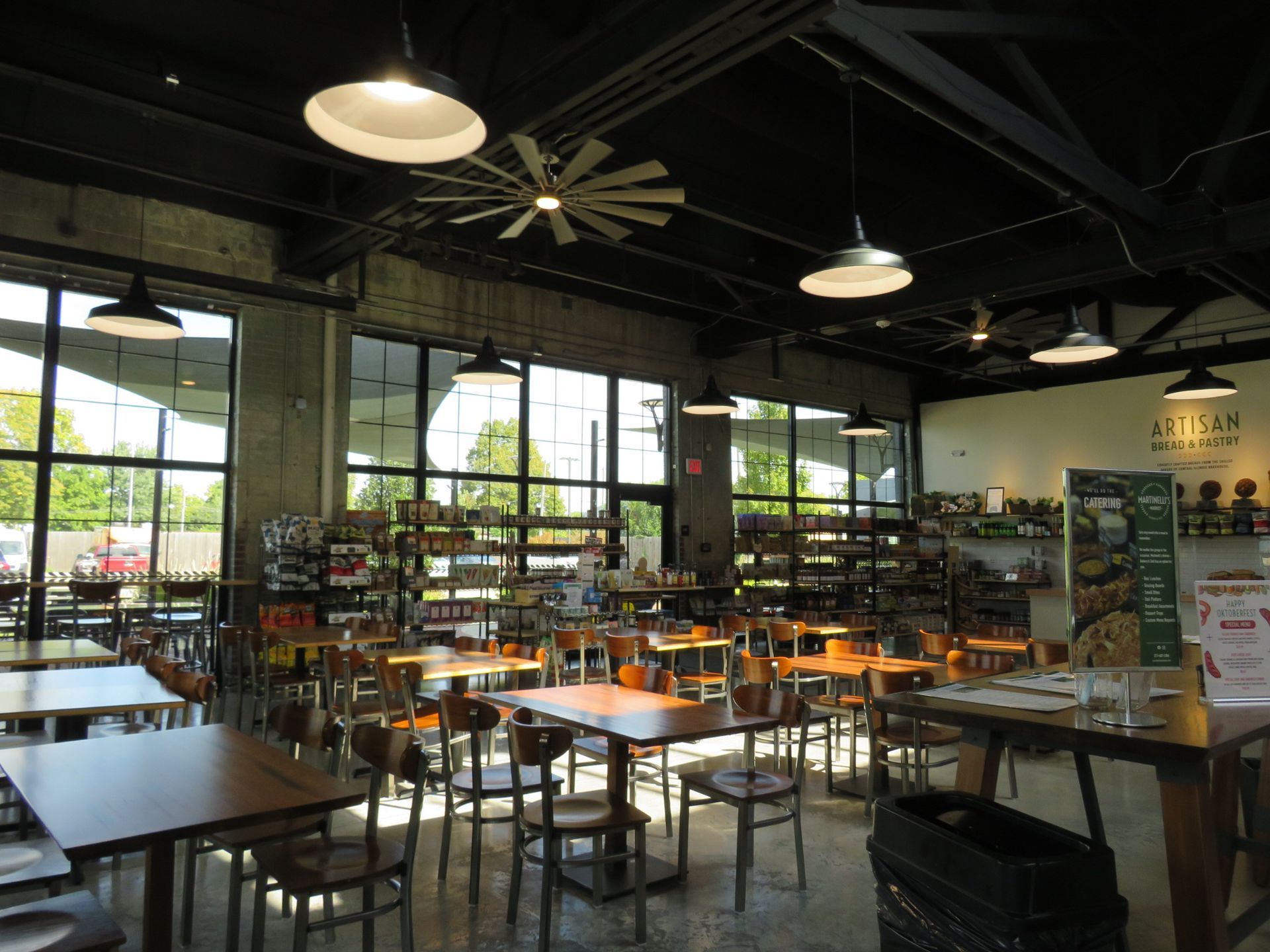 Bright café dining room with tables, chairs, large windows, and hanging lights