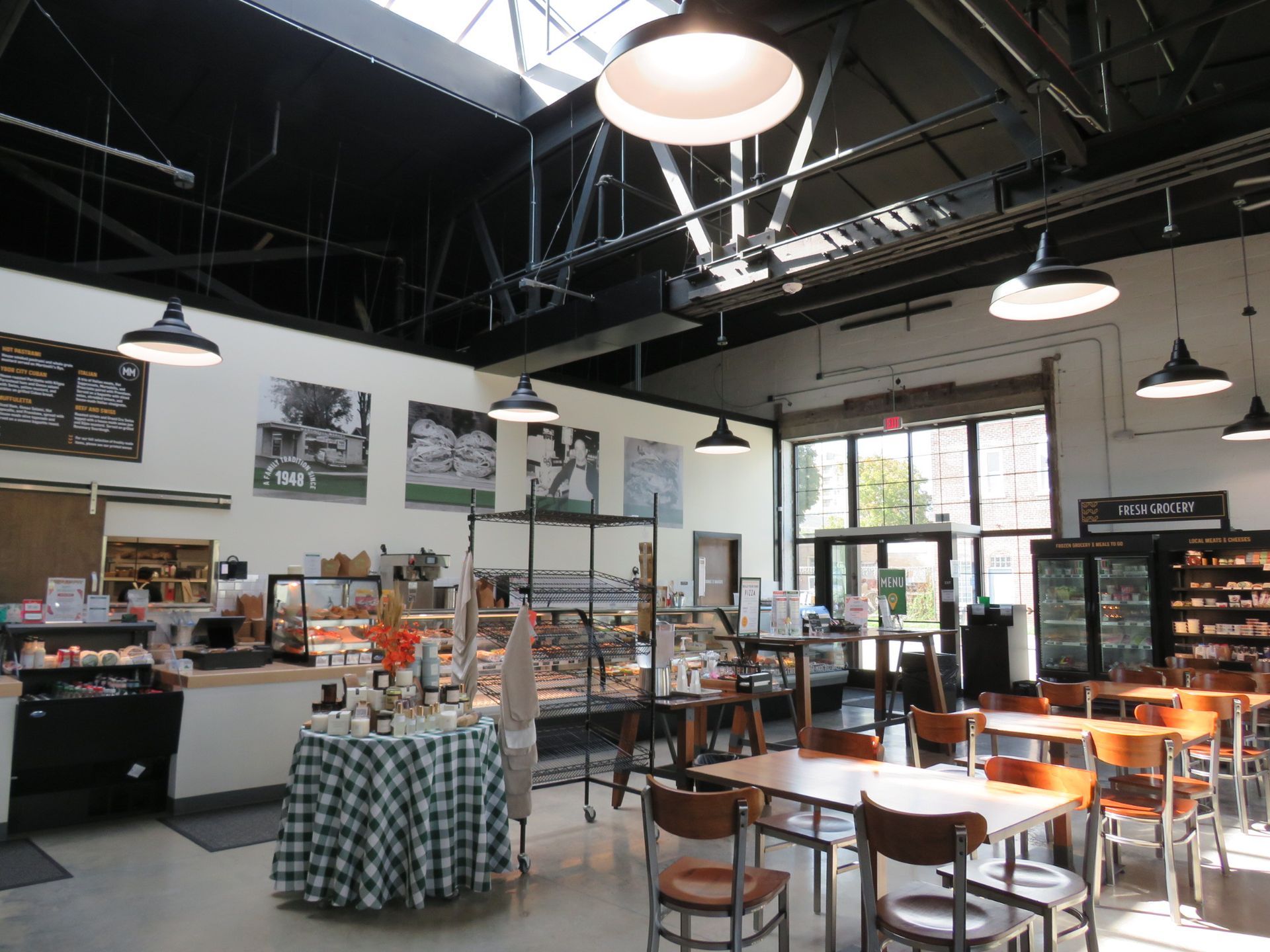 Empty cafe with wooden tables and chairs, green wall plants, and a black ceiling in a bright dining area