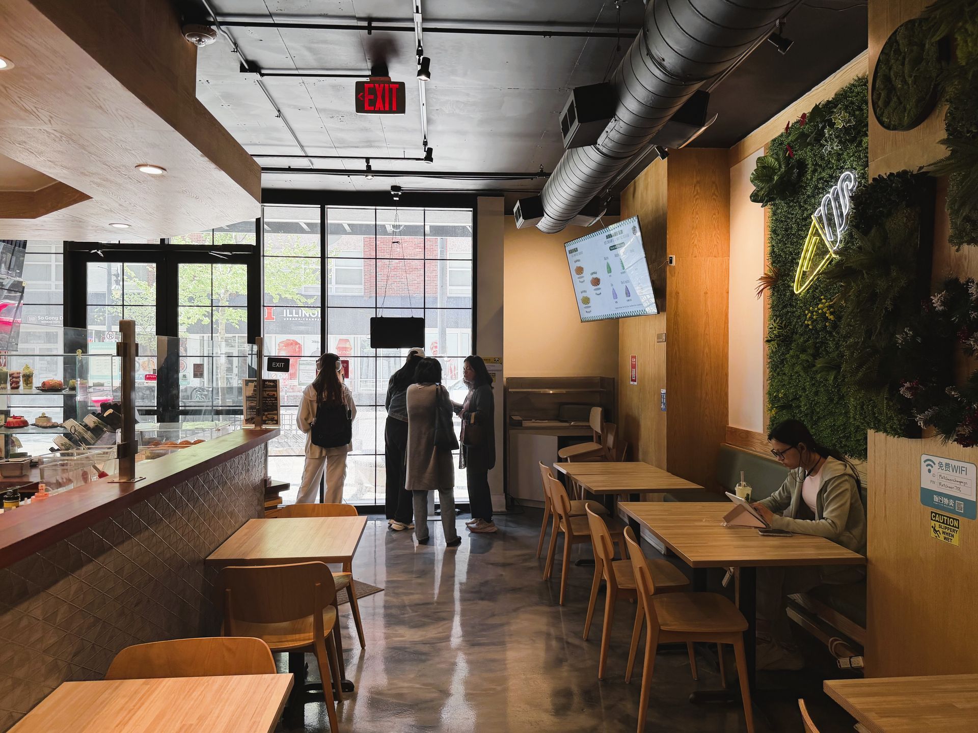 Modern café interior with tables, plants, and two people near the entrance