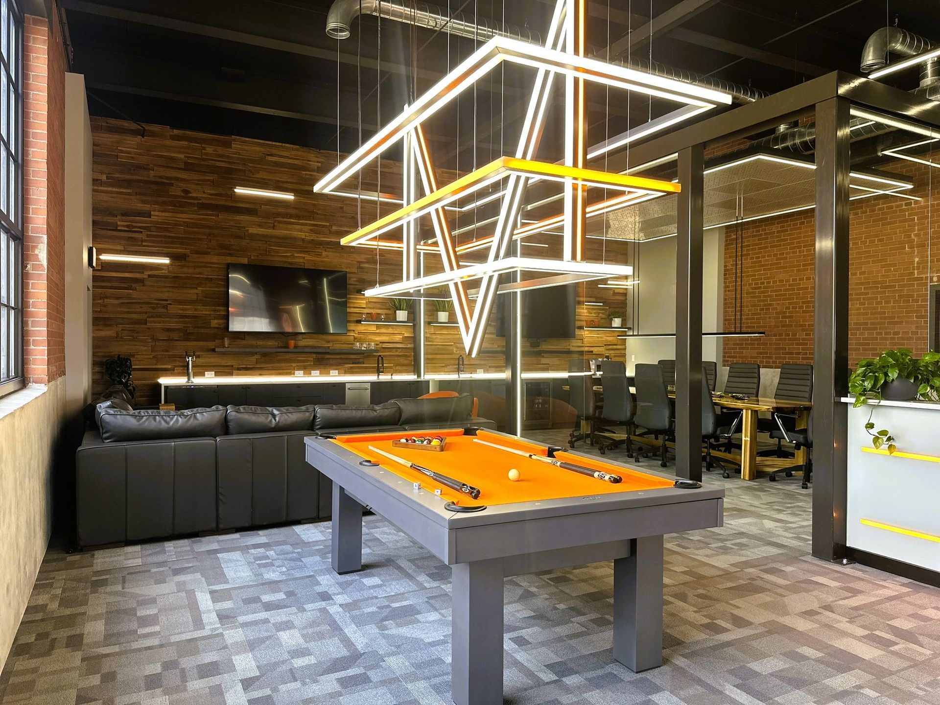 Modern game room with a pool table, black couches, brick walls, and hanging geometric lights