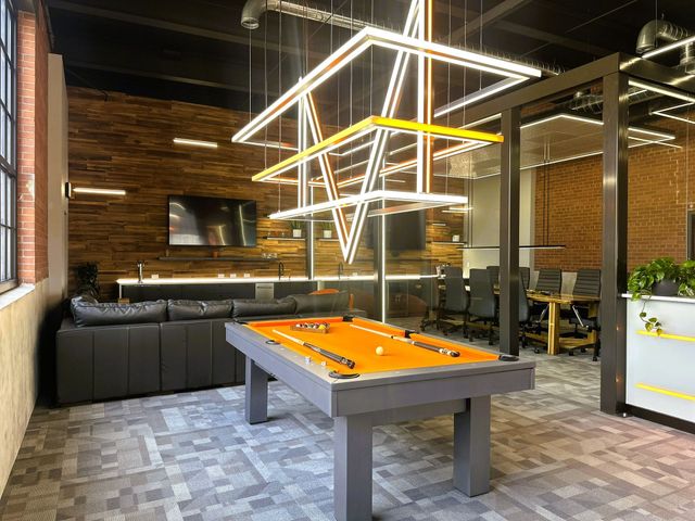 Modern lounge with a pool table, black seating, brick walls, and geometric pendant lights.