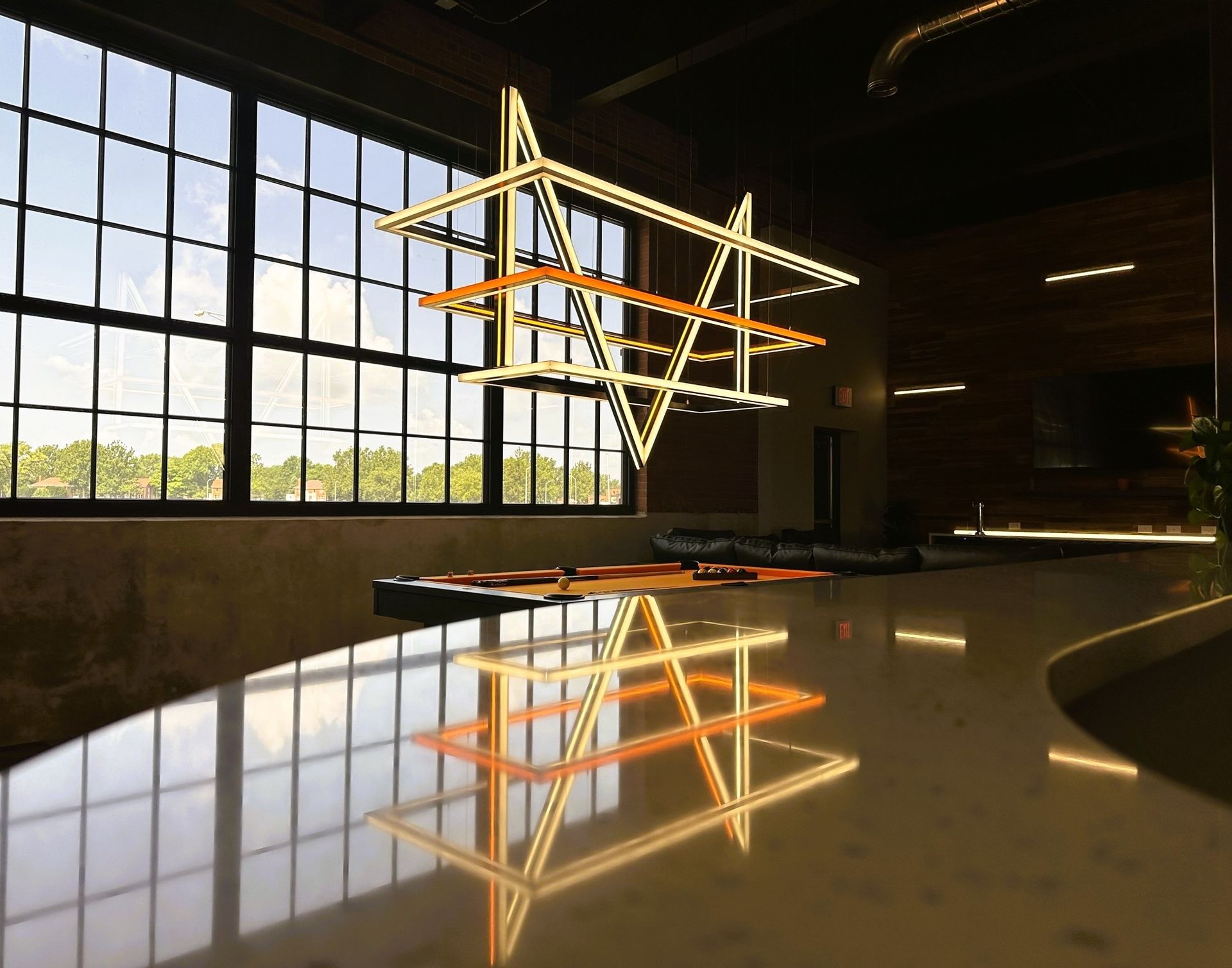 Modern lobby with a geometric hanging light sculpture reflected on a glossy floor, beside large windows.
