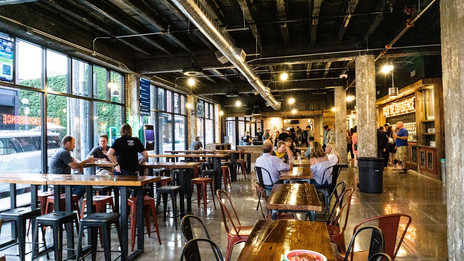 Busy modern café with patrons seated at tables under industrial lighting and exposed ceilings