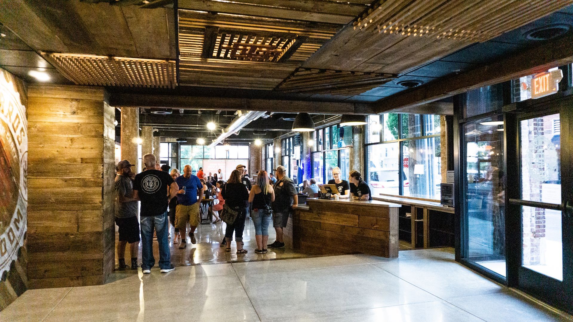 People standing in a dimly lit indoor walkway with brick walls and large windows.