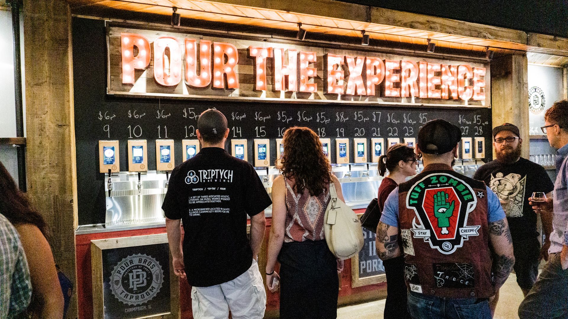 People standing at a beer counter with a glowing “Beer the Experience” sign above it.
