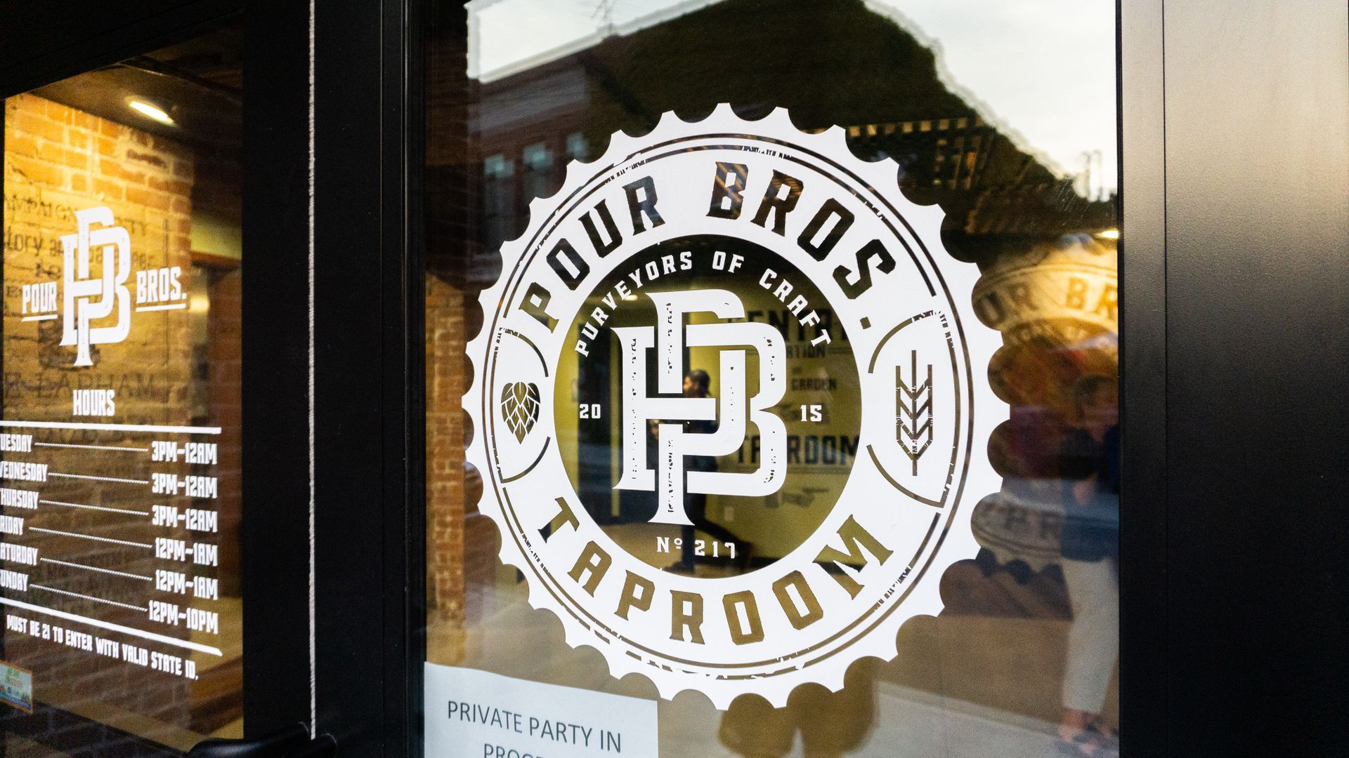 Black-and-white Pour Bros Taproom logo on a window, with menu text reflected beside it