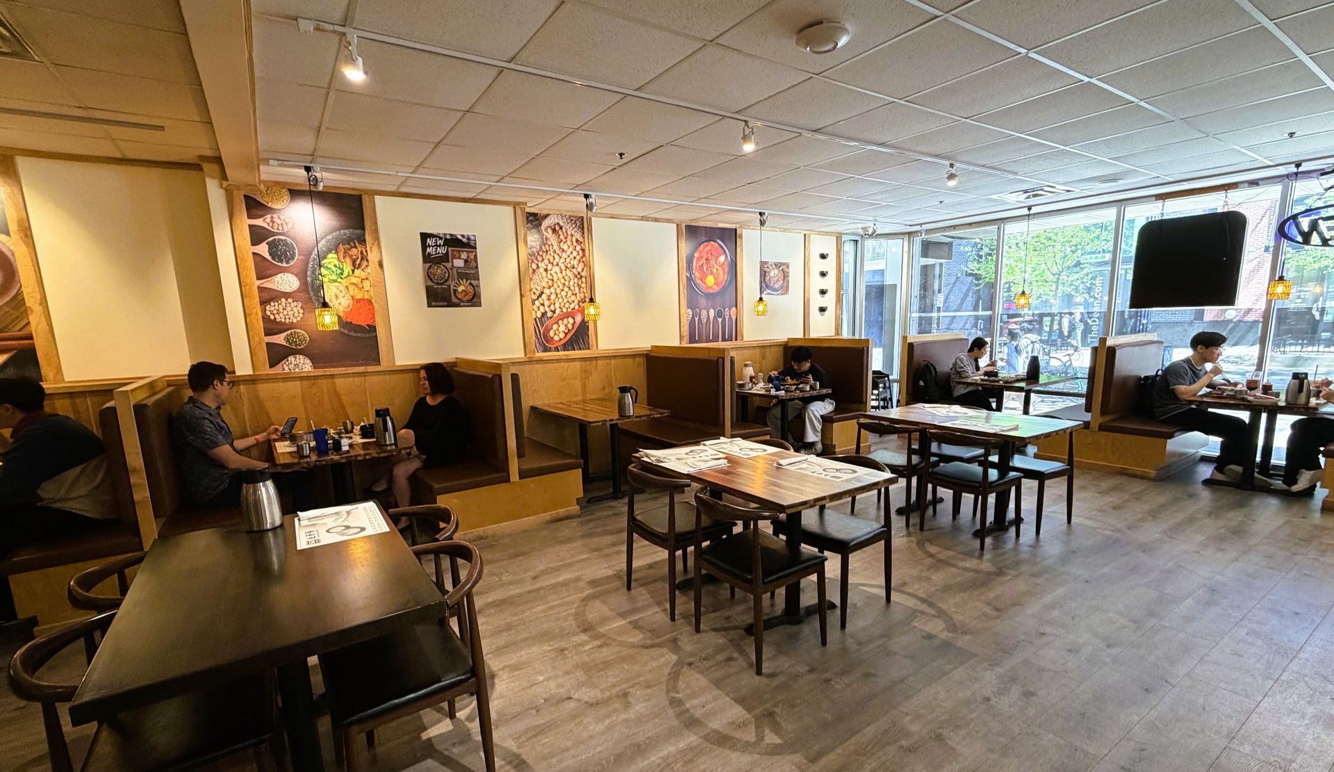 Empty café dining room with wooden tables, chairs, wall art, and daylight from large windows.