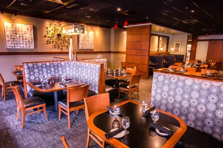 Empty modern restaurant dining area with wooden tables, patterned booths, and warm ambient lighting