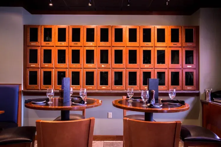 Dim restaurant booth with two tables, brown chairs, and a wall of empty wooden cubby shelves.