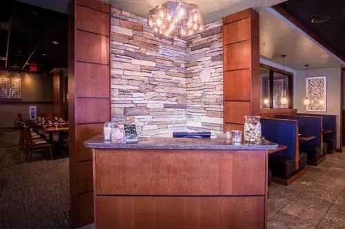 Restaurant host stand with stone accent wall, wood paneling, and booth seating in a dimly lit dining area