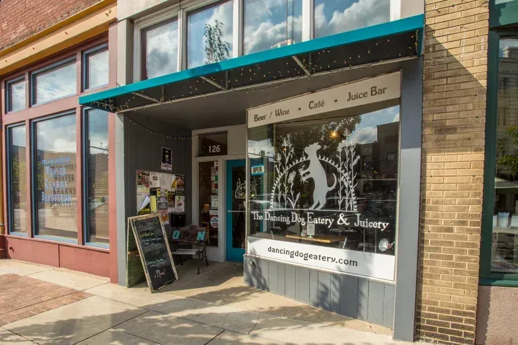 Storefront with teal awning, large windows, and a sidewalk sign on a sunny street.