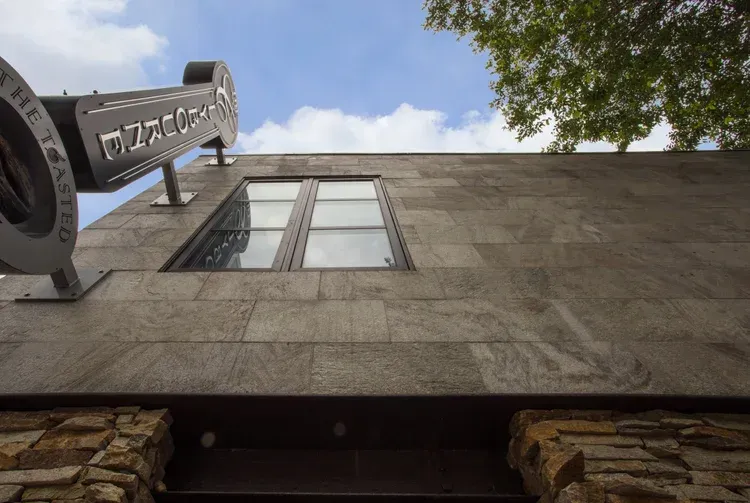 Stone building facade with tall windows and a metal sign against a blue sky, viewed from below
