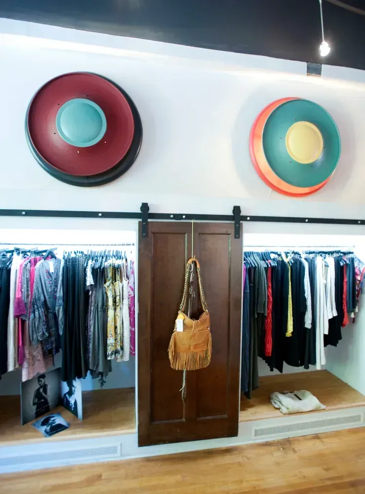 Boutique clothing display with hanging racks, central wooden doors, and colorful round wall decor