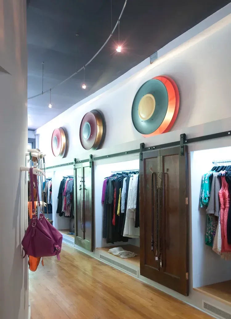 Clothing store interior with wooden floors, hanging clothes, and large colorful circular wall decor.