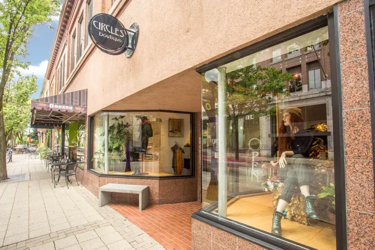 Storefront with large display windows and a sidewalk bench on a sunny street.